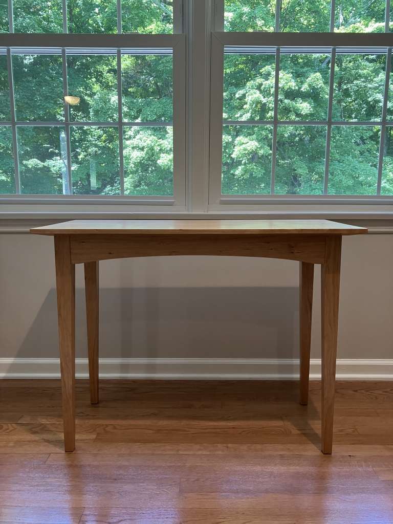 Shaker style side table made from cherry positioned below a window.