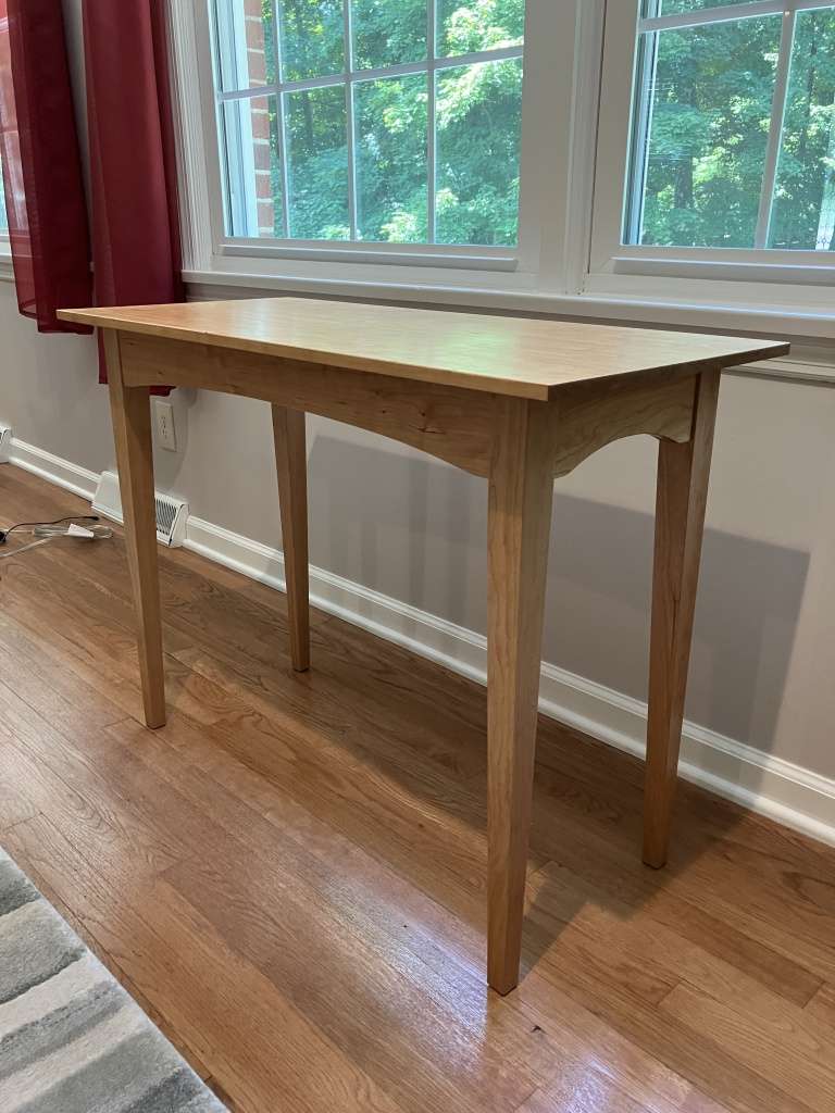 Shaker style side table made from cherry positioned below a window.