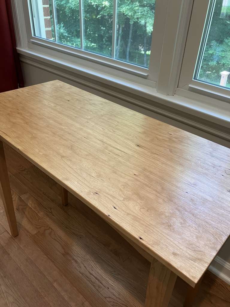 Shaker style side table made from cherry positioned below a window.