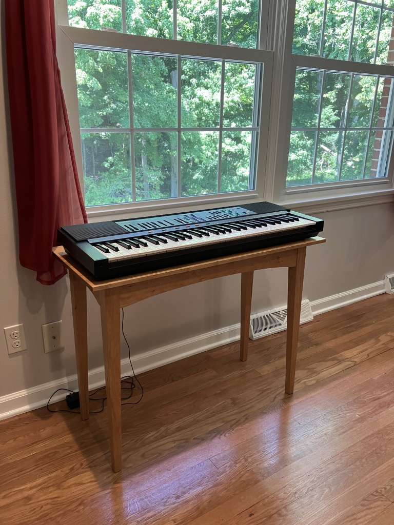 Shaker style side table made from cherry with a keyboard sitting upon it.